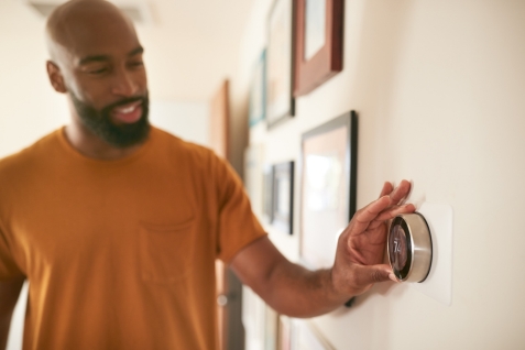 This shows a man adjusting his thermostat for a blog on keeping your home more energy efficient and lowering your heating bills during winter.