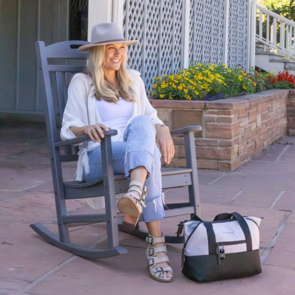 This shows someone sitting in a chair with the sterling version of the Eclipse Convertible Travel Bag near their feet.