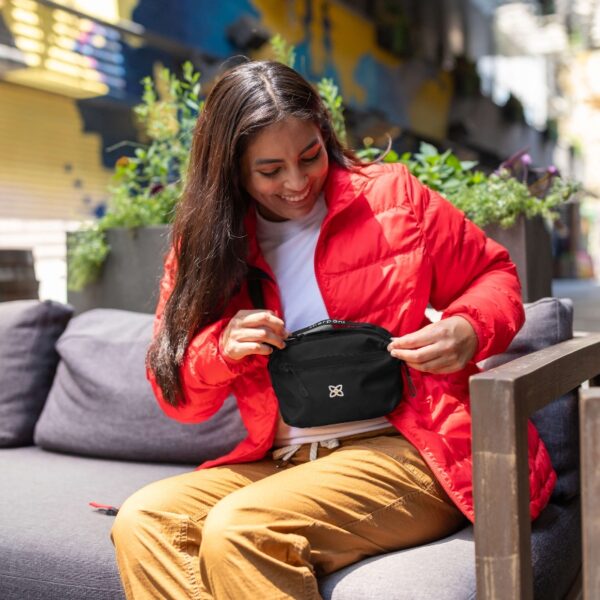 This image shows someone wearing the Hyk Hip Pack in the raven color while they go about their day outside. It's made from 100% recycled materials.