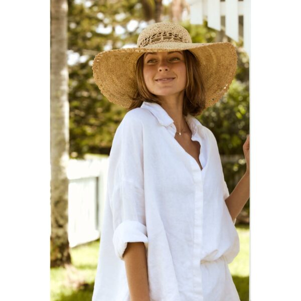This shows a woman wearing the natural colored Amy Summer Raffia Hat. The wide brim offers sun protection and the vented crown allows for cool air flow. This hat only comes in one color and one size.