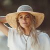 This shows a woman wearing the natural-colored Tuscany Wide Brim Straw hat. It's hand-braided with organic raffia. The wide brim offers maximum sun protection and the leather chin cord helps keep this hat in place, even on a windy day. Only offered in one size and color.